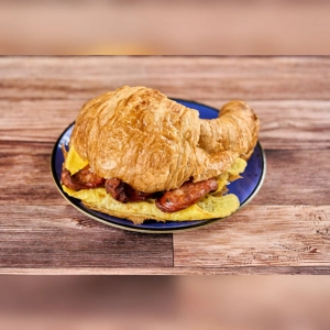 Croissant with egg and chorizo on a blue plate. The croissant is filled with visible slices of chorizo and scrambled eggs.