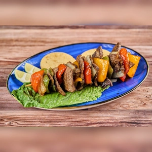 Pincho De Carne with grilled beef, red and yellow bell peppers on a blue plate. Served with lime wedges and tortillas.