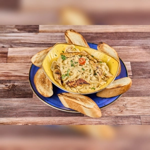 Fettuccine Alfredo with grilled chicken, garnished with parsley and cherry tomato, surrounded by toasted bread slices.