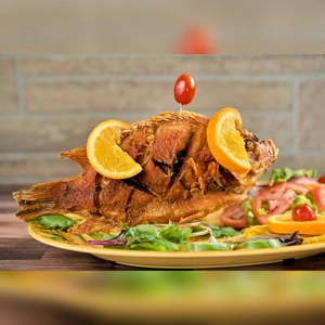 Fried Mojarra with orange slices and salad on a plate. Cuisine unknown in an unknown city.