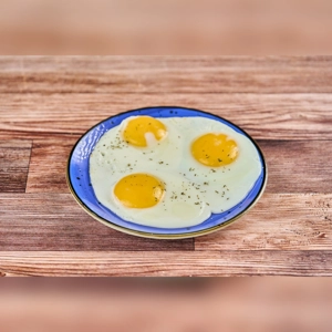 Huevos en Cacerola with three sunny-side-up eggs on a blue plate, possibly Colombian dish, city unknown.