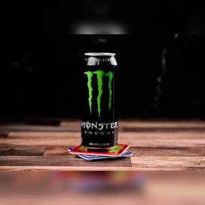Monster Energy drink can on a wooden surface with colorful coasters underneath. Unknown cuisine and city.