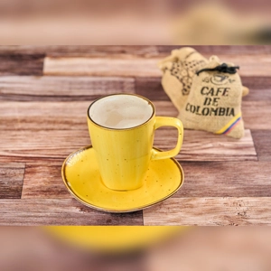 Cafe Con Leche Pequeño in a yellow cup with milk froth, next to a Colombian coffee bag.