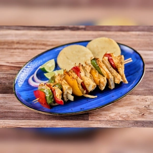 Pincho de Pollo with grilled chicken, red and green bell peppers, served with lime wedges and arepas. Cuisine type unknown.