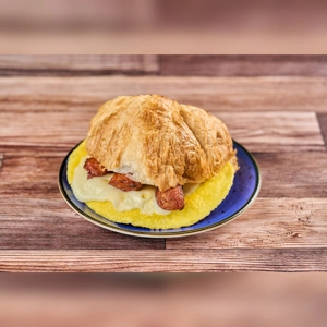Croissant with egg, cheese, and sausage on a plate. The croissant is filled with visible sausage and melted cheese. Cuisine