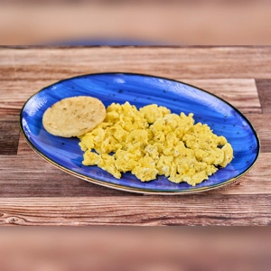 Huevos Revueltos con Arepa with scrambled eggs and a round arepa on a blue plate. Cuisine type and city unknown.