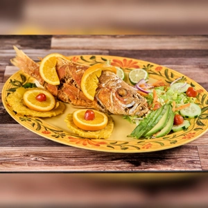 Pargo Rojo with fried plantains, orange slices, and salad on a decorative plate. Cuisine type and city unknown.