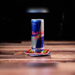 Redbull energy drink can on a wooden table with colorful coasters. Unknown cuisine and city.