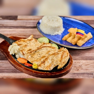 Grilled chicken breast with visible cauliflower and carrots, accompanied by rice and yuca fries, Colombian cuisine.