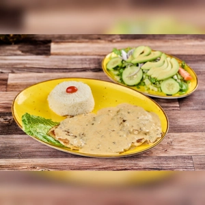 Pechuga al Ajillo with creamy garlic sauce, rice, and salad with avocado and cucumber. Cuisine type and city unknown.