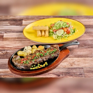 Skirt steak with grilled peppers and cauliflower, served on a wooden platter. Includes a side salad with avocado and yuca