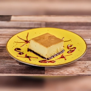 Flan on a yellow plate with caramel topping and decorative syrup. Unknown cuisine type and city.