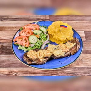 Mar y Tierra with grilled steak, shrimp, plantains, and salad on a blue plate. Cuisine type and city unknown.