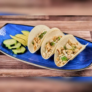 Taquitos de Pollo with shredded chicken and cilantro on a blue plate, served with sliced cucumber and avocado. Mexican