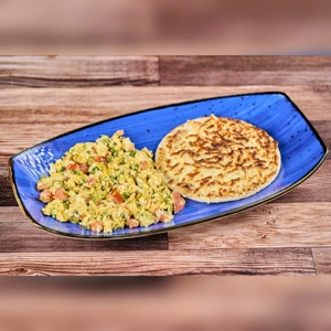 Arepa Tela with cheese and scrambled eggs with tomatoes and green onions on a blue plate. Cuisine type and city unknown.