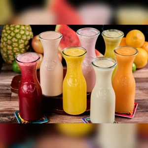 Batidos En Leche with various fruit flavors in glass bottles. Visible fruits include pineapple and watermelon. Cuisine type