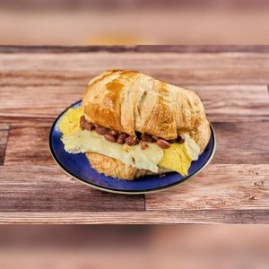 Croissant with egg, cheese, and beans on a blue plate. The croissant is golden brown, with visible melted cheese and cooked