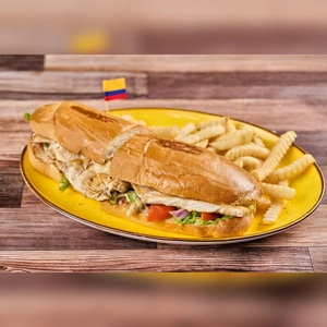Chicken Sandwich with lettuce, tomato, and crinkle-cut fries on a yellow plate. Colombian flag toothpick is inserted.