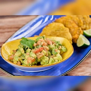 Guacamole with visible avocado and tomato, served with tostones on a blue plate. Cuisine type and city unknown.