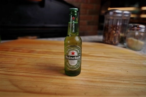 Heineken beer bottle on a wooden table. The green glass bottle is unopened and has condensation. Visible in a restaurant