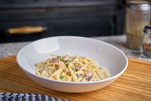 Linguine alla Carbonara with visible bacon and peas in a creamy sauce, served in a white bowl.