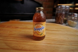 Snapple 16 oz bottle of peach iced tea on a wooden surface.
