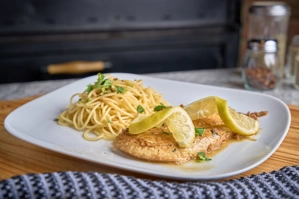 Chicken Francese with lemon slices and spaghetti on a white plate, served in New York.