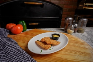 Chicken tenders with crispy breading, served with a small cup of yellow dipping sauce on a white plate.