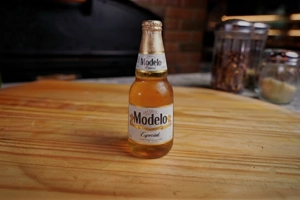 Bottle of Modelo Especial beer on a wooden surface, with a clear glass bottle and a gold label in New York.