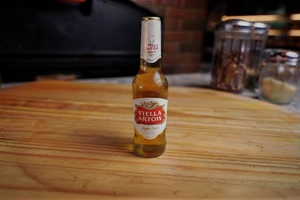 Stella Artois beer bottle on a wooden table, with a brick wall and jars in the background.