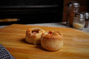 Rolls with visible cheese and ham on a wooden board. Cuisine and city unknown.