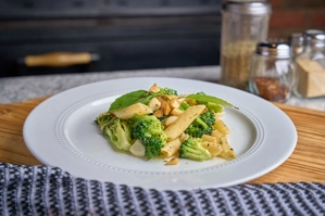 Penne broccoli dish with visible penne pasta, broccoli florets, and garlic on a white plate. Cuisine type and city unknown.