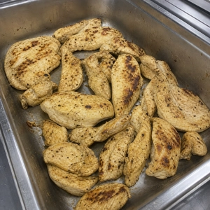 Grilled chicken breast with visible seasoning in a metal tray at Buffet Latino BBQ in Carrollton.