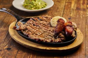 Plato a la agucatala with grilled sirloin steak, fried plantains, and a side of guacamole in Astoria.