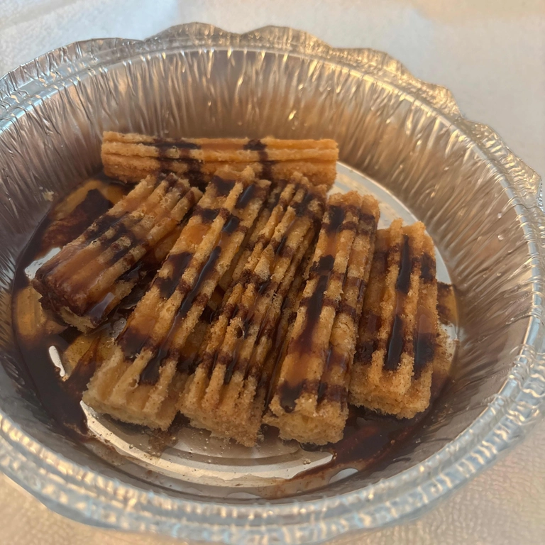 Churros with chocolate drizzle in a foil container, a Spanish dessert in Roanoke.