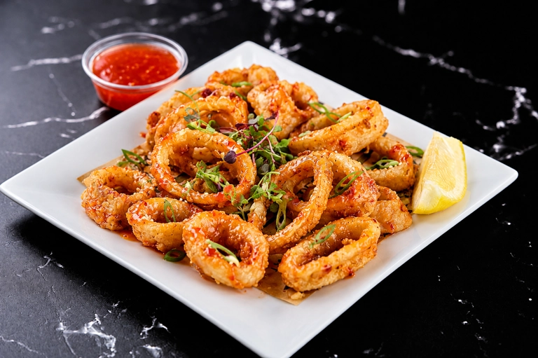 Fried Calamari in a Sweet Chili Sauce with lemon wedge and microgreens, served in a Cuban restaurant in Moonachie.