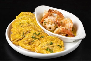 Camarones al ajillo con tostones en un plato blanco. Cocina desconocida en ciudad desconocida.