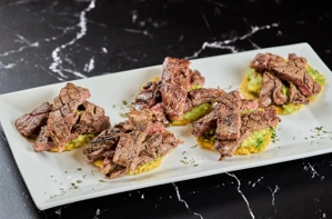 Montaditos de churrasco con carne asada y aguacate sobre tostones. Cocina desconocida en ciudad desconocida.