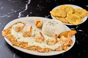 Pechuga marinera con camarones y salsa blanca, acompañada de arroz y plátano frito. Cocina desconocida en ciudad desconocida.