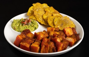 Guacamole con chicharrones y tostones en un plato. Se ven chicharrones dorados, tostones crujientes y guacamole con pico de