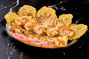 Plato Mar y Chicken con pollo a la parrilla, camarones y tostones en un plato negro. Cocina desconocida en una ciudad